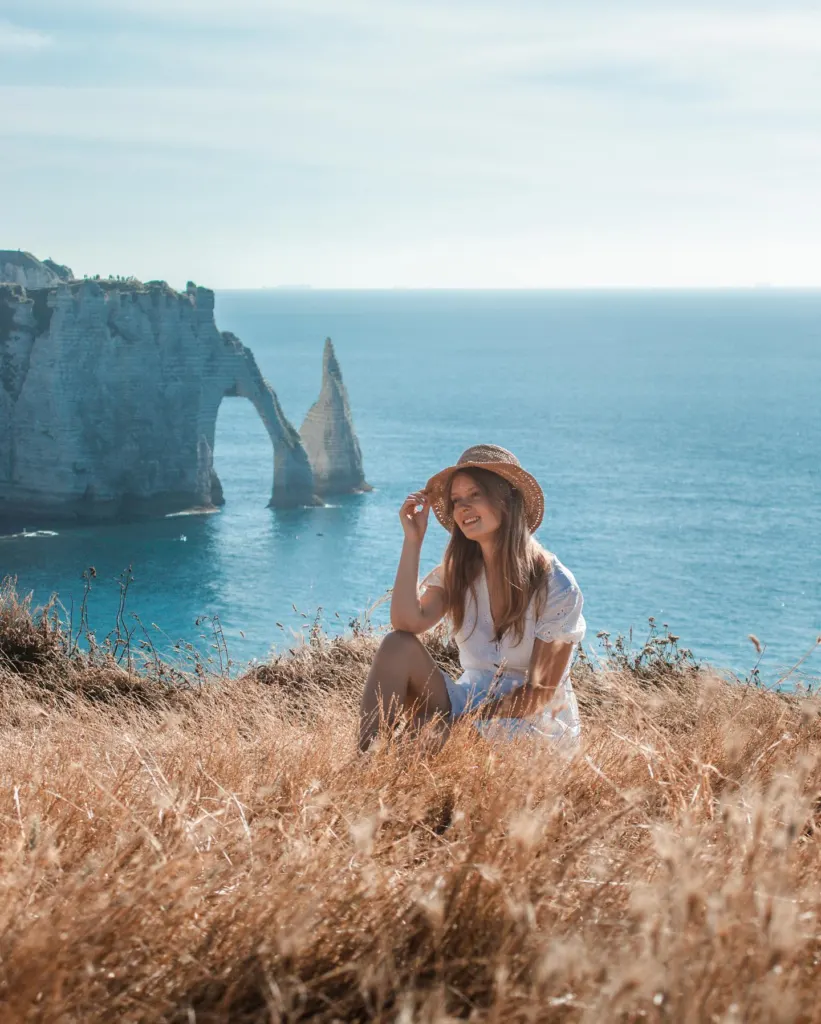 Woman in a straw hat at Etretat with the white cliff and sea arch behind