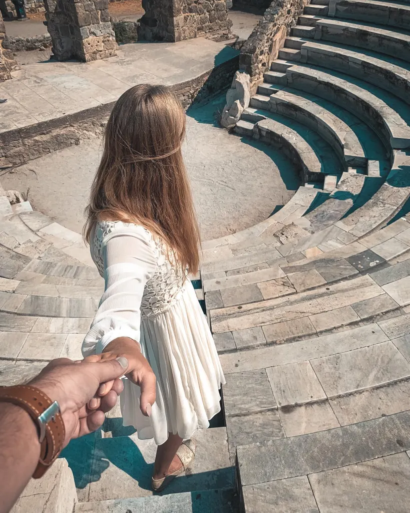 Woman holding her partner's hand on the stone seating steps of an ancient theatre on Kos