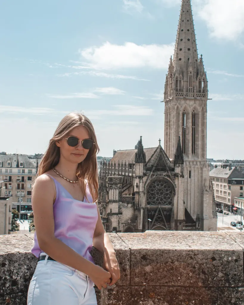 Woman on a stone wall in front of a Gothic church tower in a Normandy town