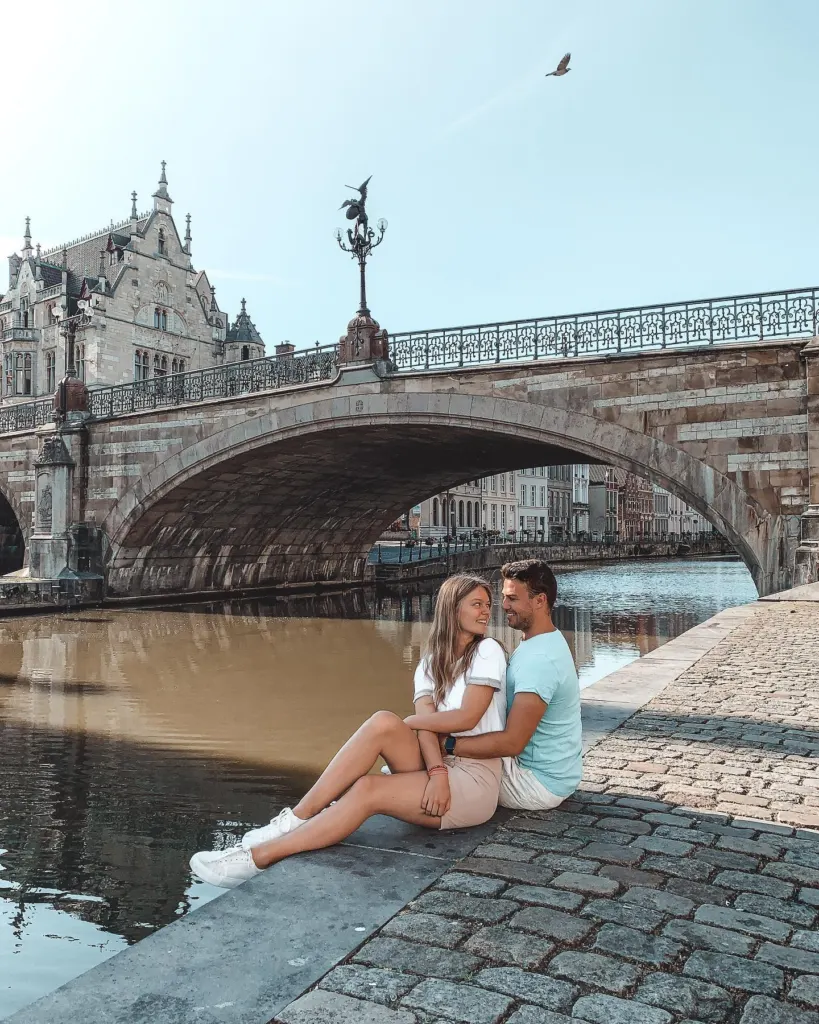 Couple sitting on a stone ledge by a bridge over the water in Ghent's old centre