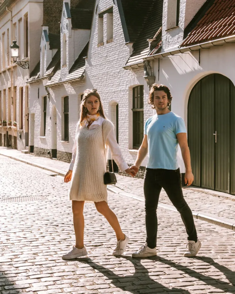 Couple walking hand in hand down a cobbled Bruges street with white gabled houses