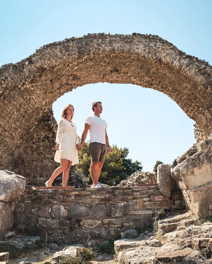 Couple standing together inside an old stone arch among ruins on Kos