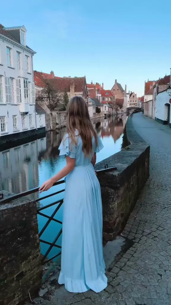 Woman in a blue dress at a canal in Bruges with brick houses